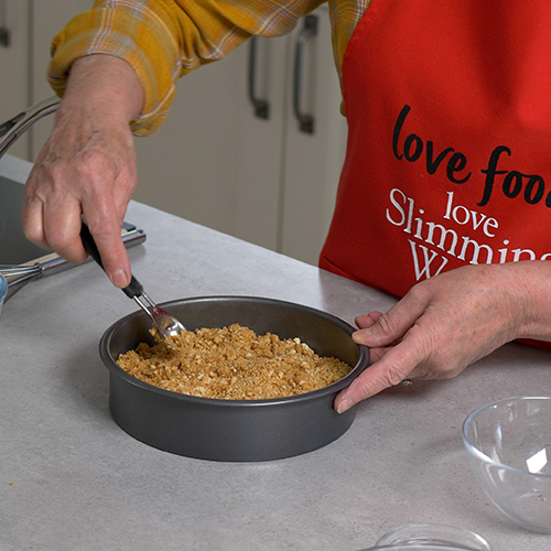 Slimming World chef flattening biscuit cheesecake base with spoon
