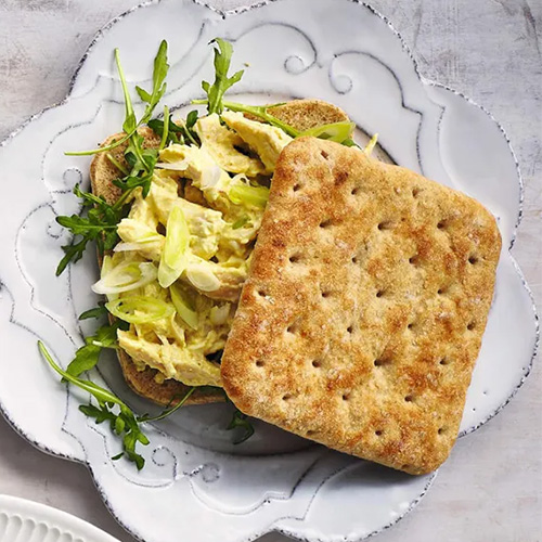 Slimming World Coronation chicken sandwich. The sandwich is served on a white plate with a floral design. The background is light grey.