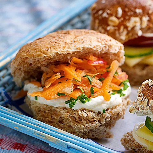Slimming World Fruity slaw sandwich. The sandwich is made up of a wholemeal roll filled with Quark and a carrot slaw. The sandwich sits in a light blue basket, which rests on a white tablecloth.