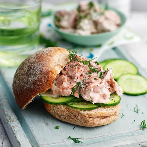 Slimming World Tuna marie rose and cucumber sandwich. The sandwich is made up of a wholemeal roll, slices of cucumber and tuna. It sits on a light blue chopping board.